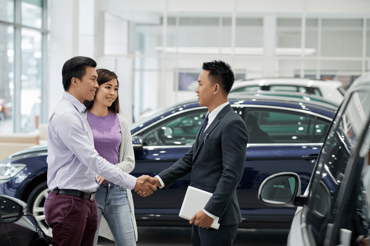 man and woman shaking hands and talking to car dealer