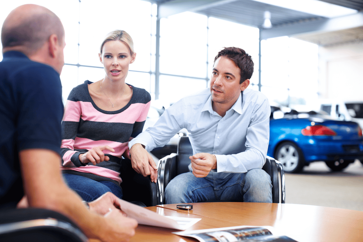 man and woman sitting across a man talking in car dealership