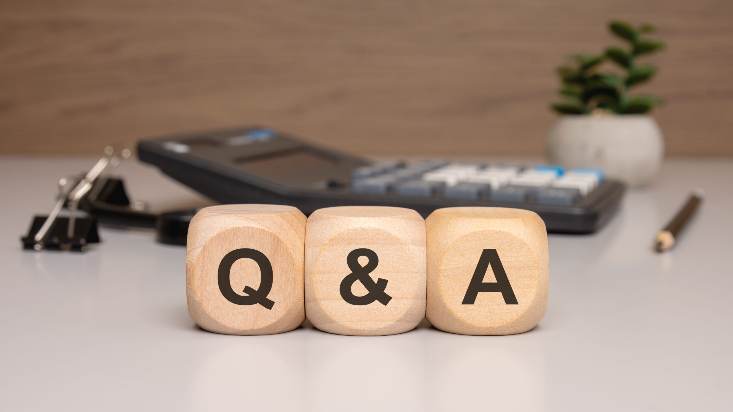 wooden blocks spelling q placed clean office desk with calculator pencil small plant scaled